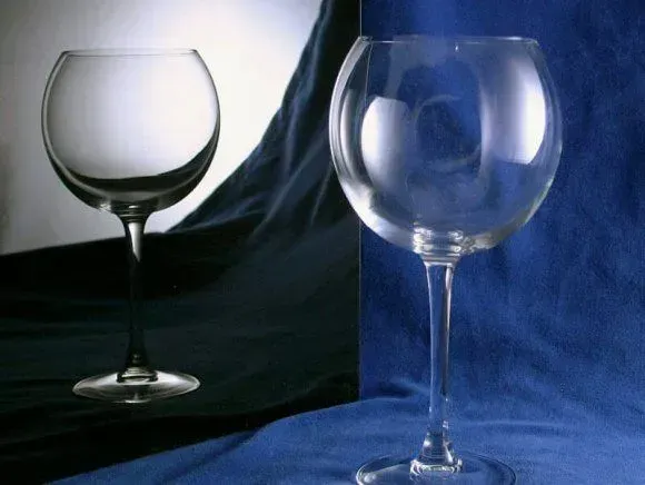 A clear glass goblet sits on a blue fabric surface, reflected against a split background of dark and light panels.