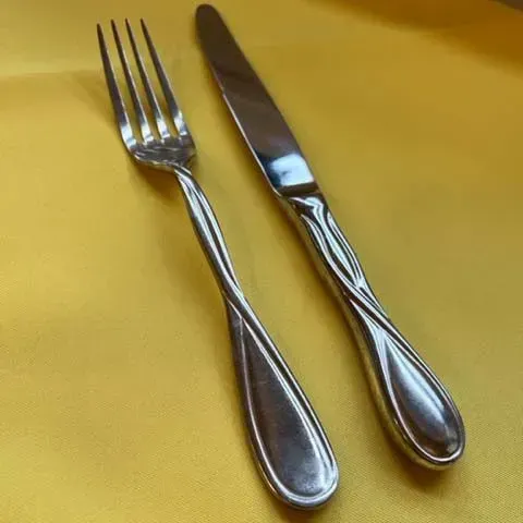 A stainless steel fork and knife with a decorative twisted handle design, resting on a plain yellow surface.