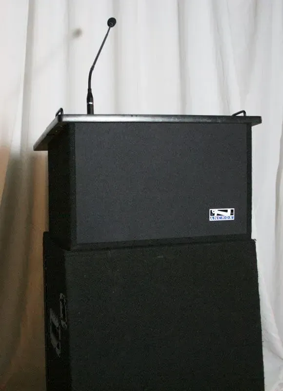 A black podium with a microphone attached to the top, standing in front of a white draped background.