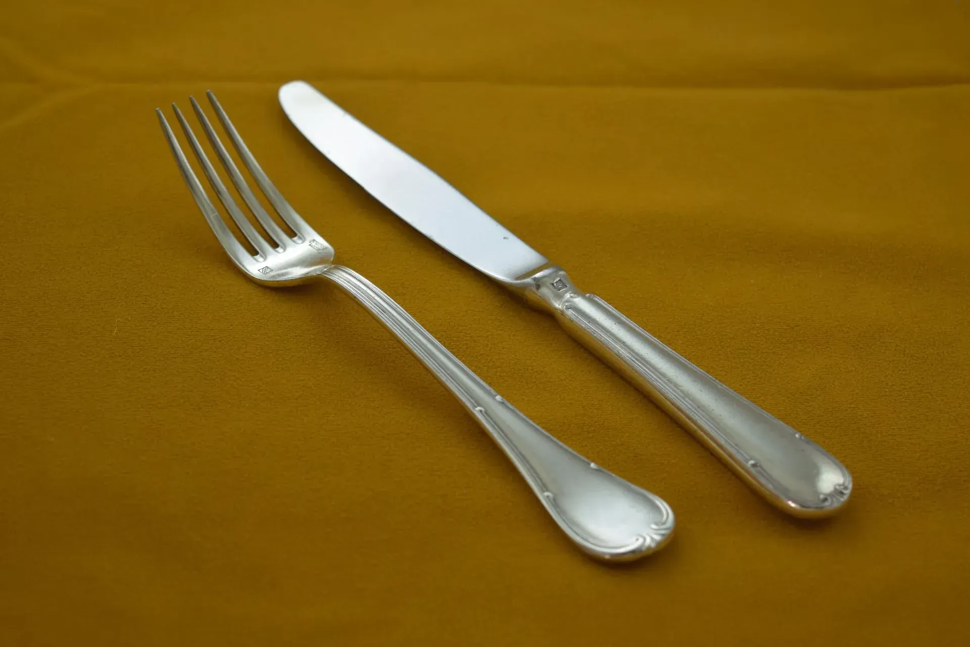 A silver dinner fork and knife laid side by side on a plain mustard-yellow background.