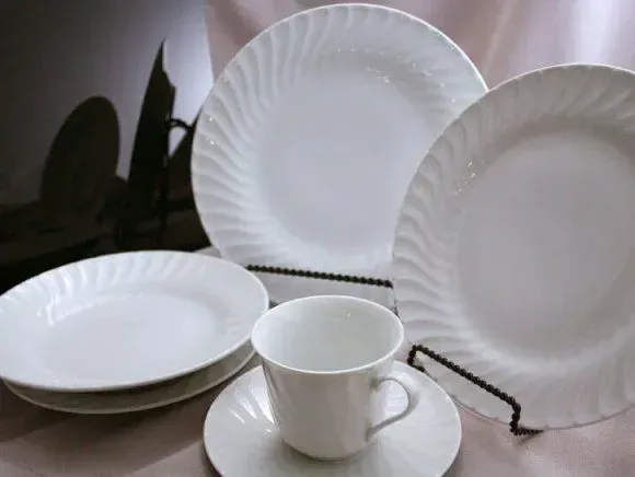 A set of white, swirl-patterned ceramic dishes, including dinner plates, a saucer, and a cup on a neutral surface.