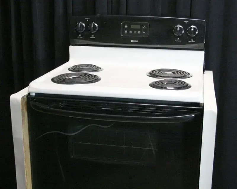 Black electric stove with four coil burners and oven door in a kitchen setting