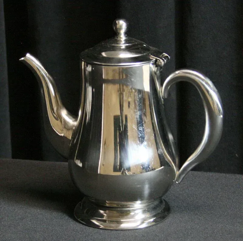Polished silver teapot with lid and curved spout on a dark background