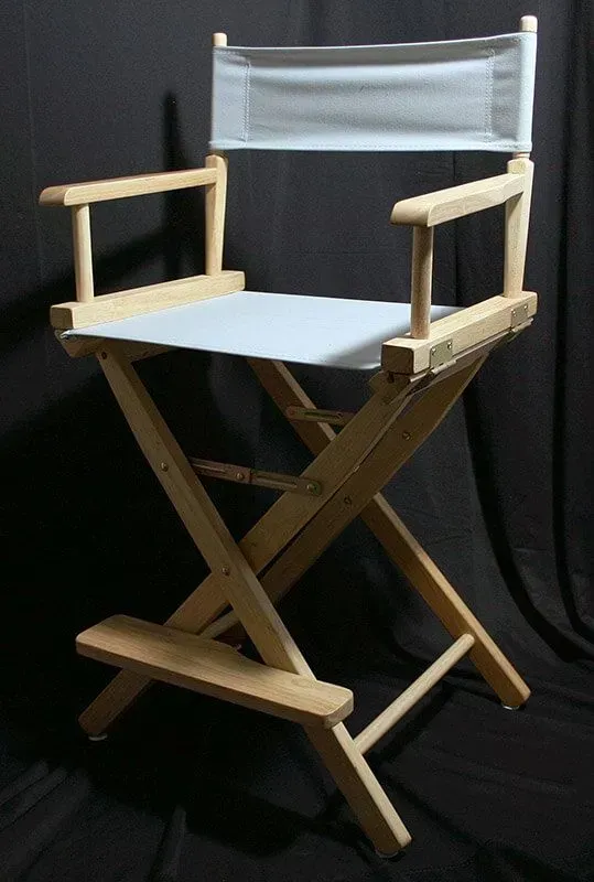 A wooden director’s chair with a light gray canvas seat and back, set against a dark background.