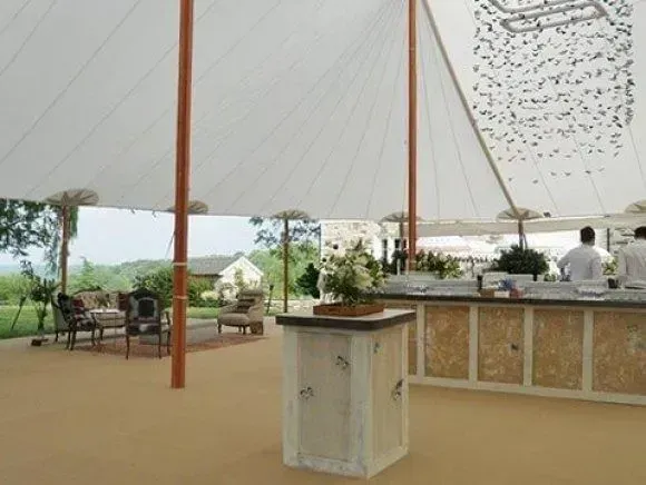 An event tent with a bar, seating area, and floral centerpiece, overlooking a green landscape.