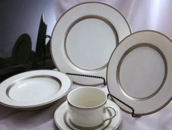 A set of white fine china featuring a wide, metallic silver rim, including plates, a saucer, and a tea cup.