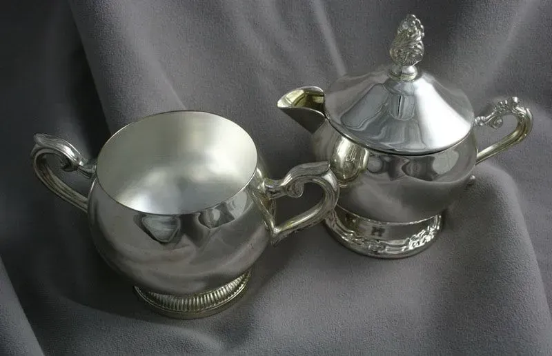 Two silver decorative sugar bowls on gray fabric, one open and one lidded