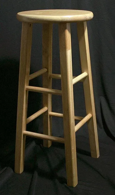 A wooden bar stool with four legs and two levels of crossbars, set against a plain dark background.