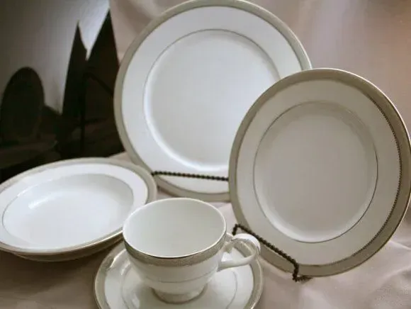 A place setting of white fine china with simple tan bands, including plates, a bowl, and a teacup on a saucer.
