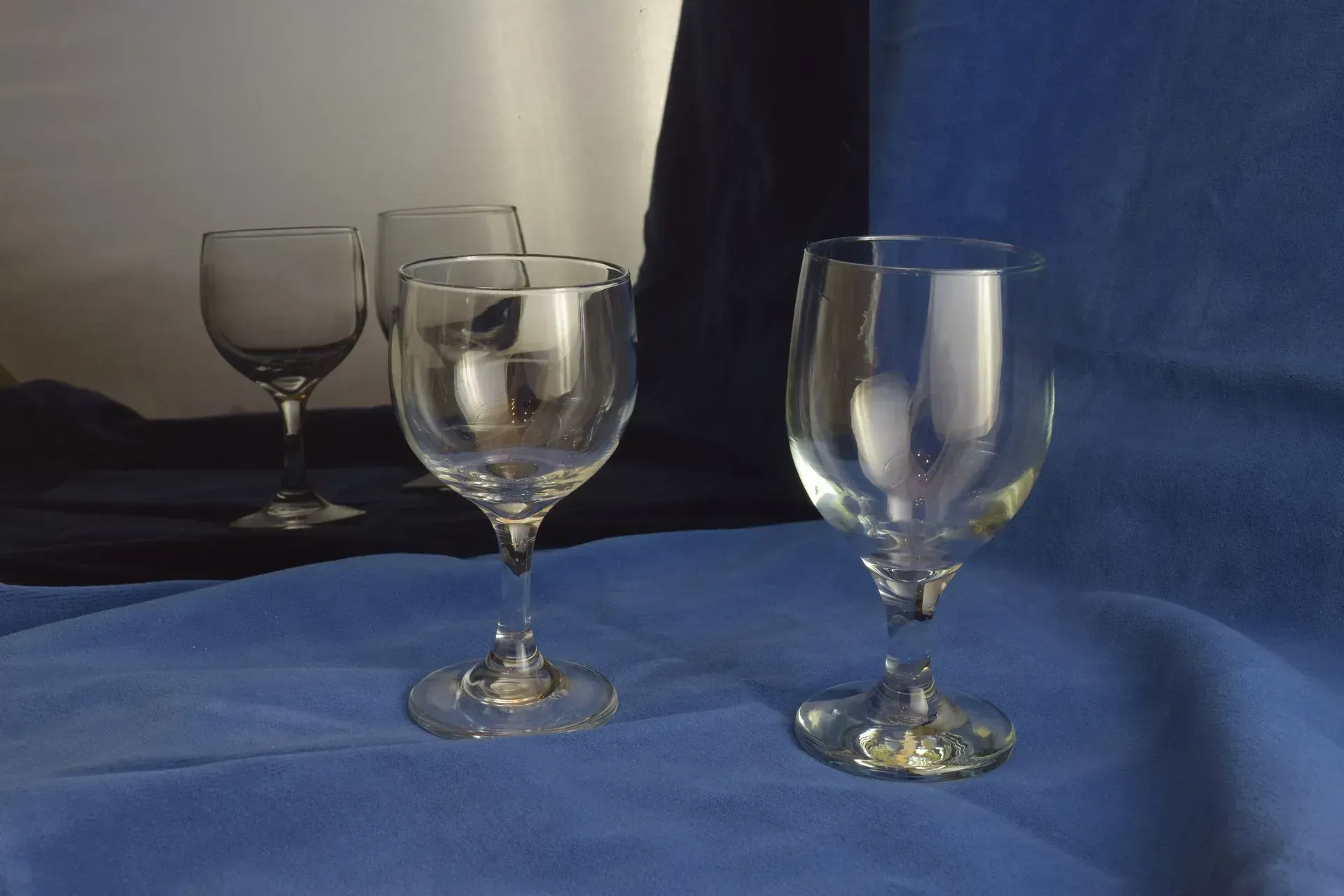 Three clear glass goblets stand on a blue surface, with a dark blue and white backdrop.