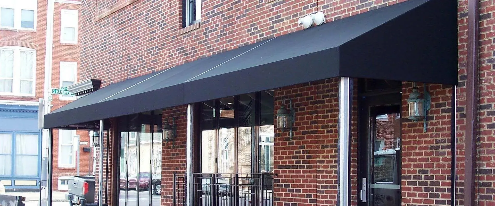 A black fabric awning extends over the brick entrance of a storefront with glass doors and metal support poles.