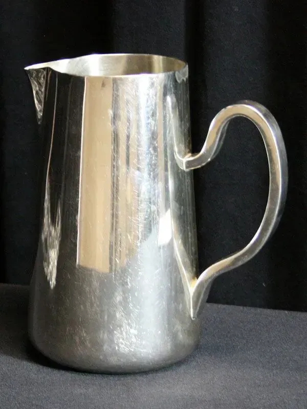 Silver metal pitcher with a curved handle on a dark surface