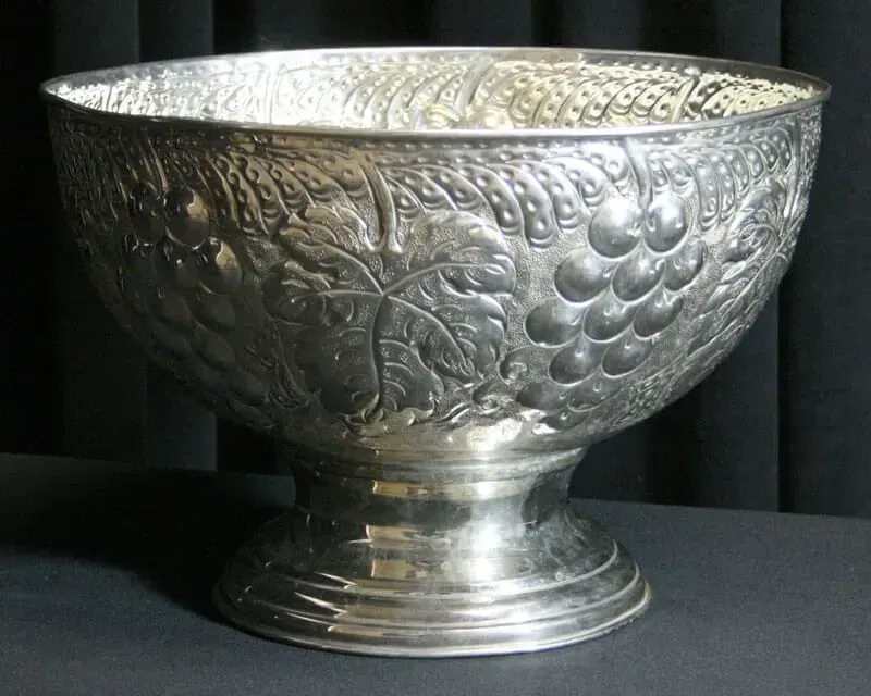 Silver embossed decorative bowl with floral and grape patterns on a dark background