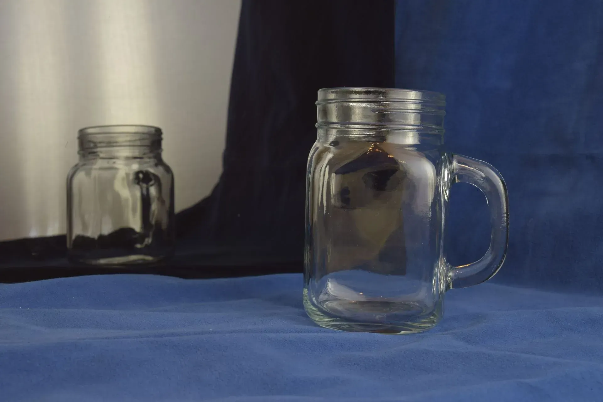 Two clear glass mason jar mugs sitting on a blue cloth against a background of black and blue curtains.