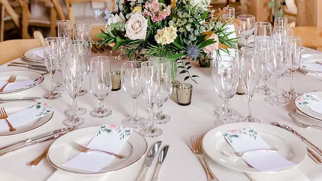 A formal round table set for a wedding with floral centerpieces, white plates, crystal glasses, and printed menus.