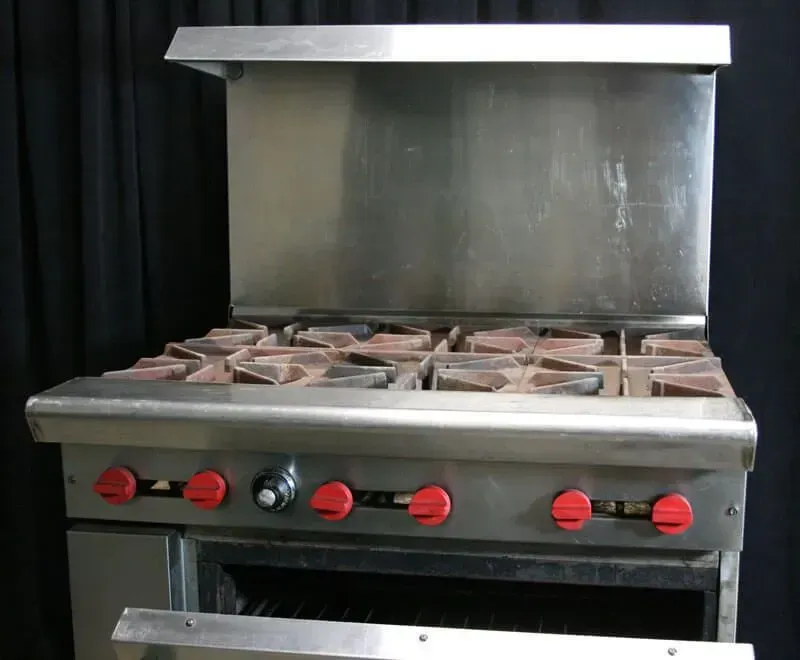 Stainless steel commercial stove with red knobs and pans on burners under a metal hood