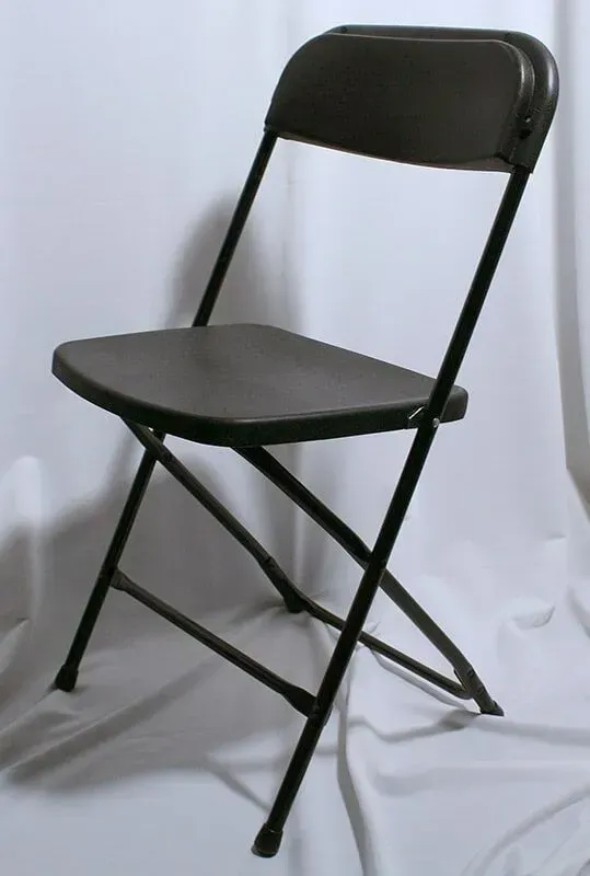 A black metal folding chair stands on a white draped surface.