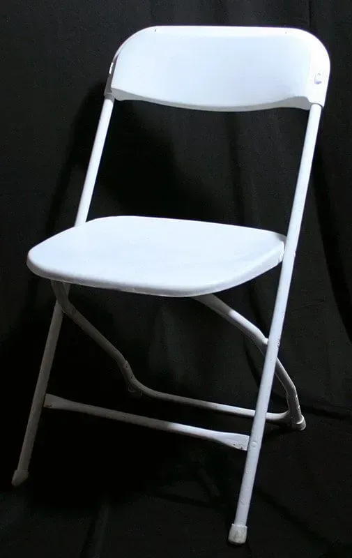 A white, metal folding chair centered against a plain black background.