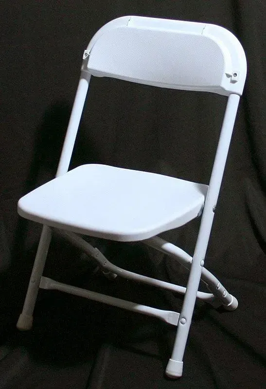A white, metal folding chair set against a dark background.