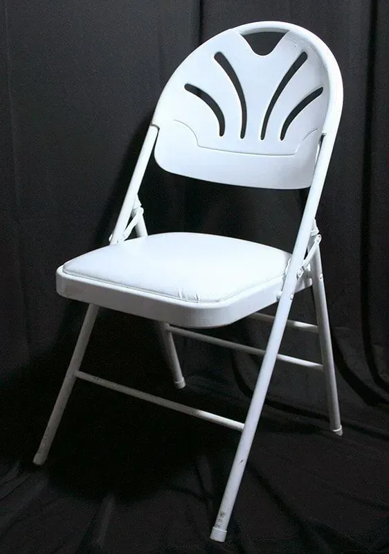 A white folding chair with a fan-shaped backrest and a padded seat, set against a dark background.