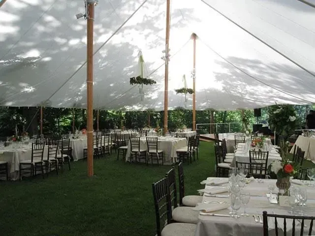 Tables set for a wedding reception under a large white marquee tent on a grassy lawn.