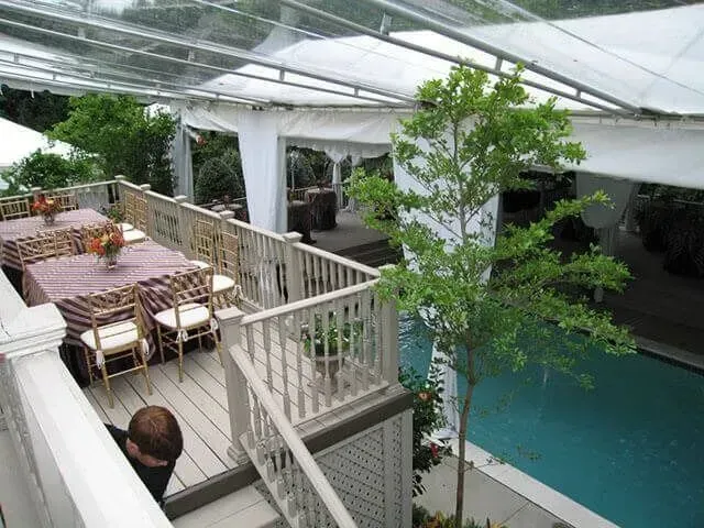 An outdoor deck with tables set for an event overlooks a swimming pool covered by a large white tent structure.