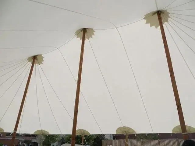 Interior view of a white, high-peak event tent supported by tall wooden poles.