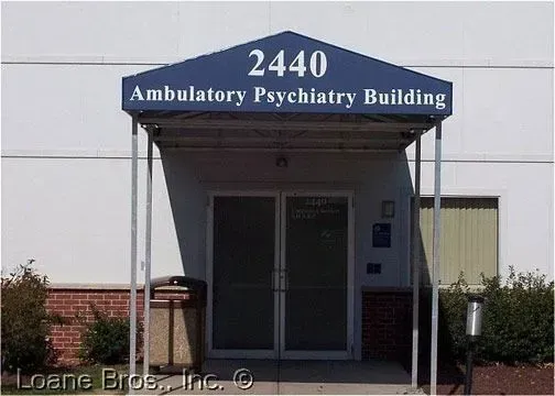 Entrance to the 2440 Ambulatory Psychiatry Building with a blue awning over double glass doors and brick accents.
