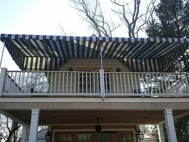 A two-story house exterior features a balcony with a black and white striped retractable awning above the doorway.