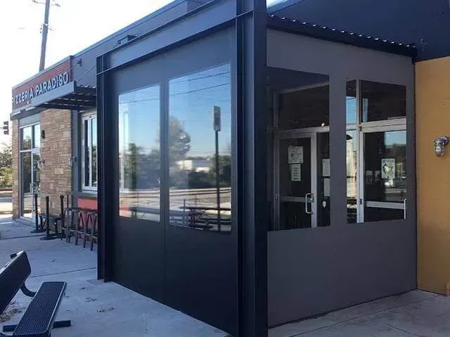 A black metal frame structure with clear vinyl window panels enclosing the entrance area of a building.