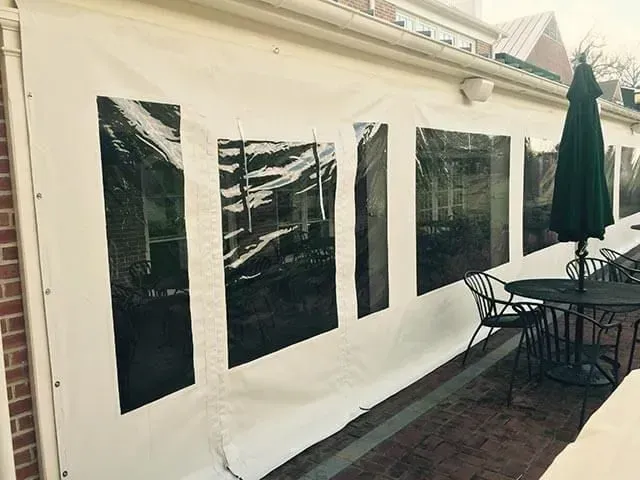 Outdoor patio with a white heavy-duty vinyl enclosure featuring clear windows, next to a black table and matching chairs.