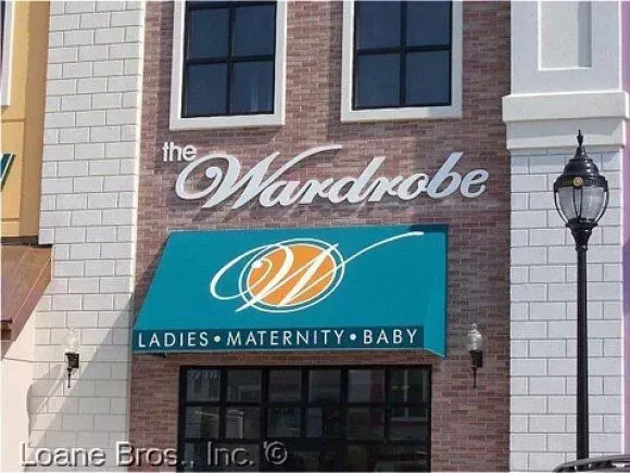 Storefront for The Wardrobe, a shop selling ladies', maternity, and baby apparel, with a teal awning and brick facade.