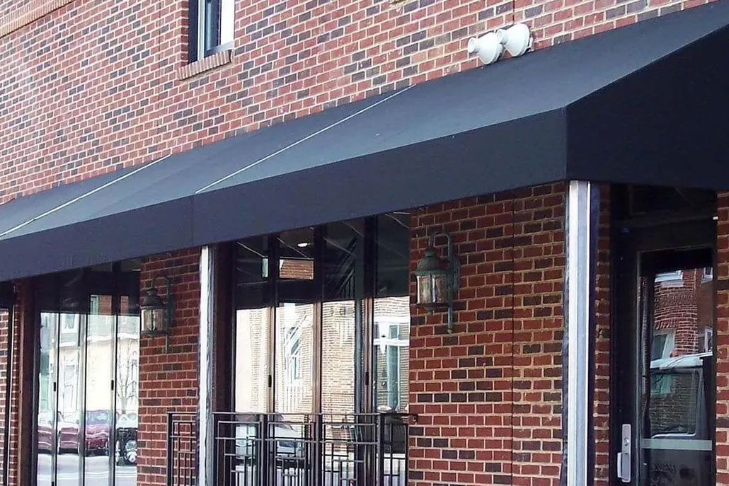 A black fabric awning extends over the brick exterior of a storefront featuring glass doors and metal posts.