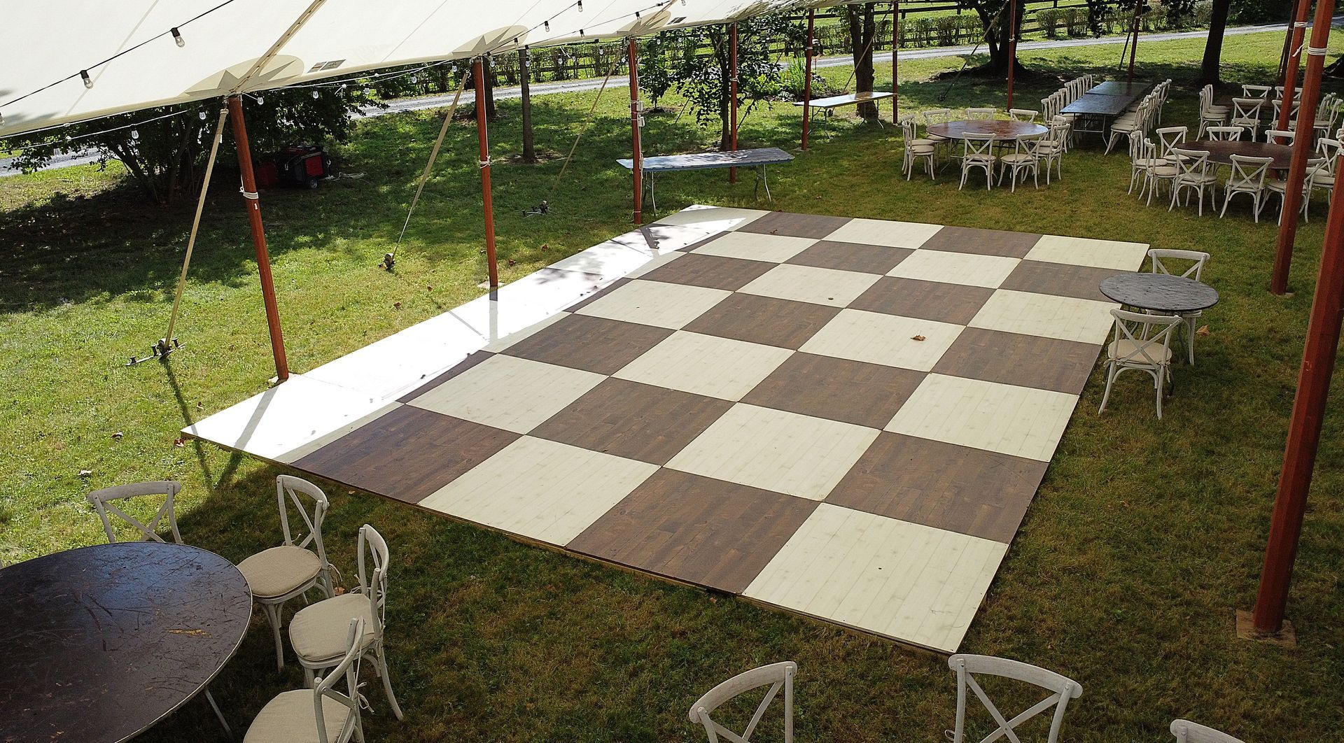 Outdoor stage with a large brown-and-white checkerboard mat under red poles on a grassy lawn