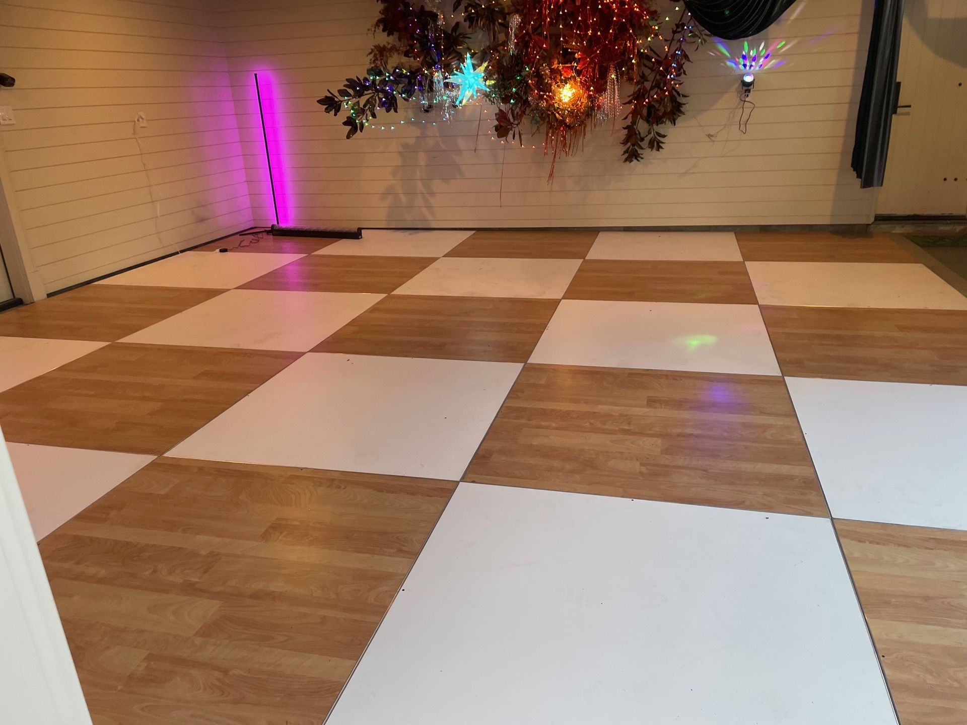 Empty dance floor with white and wood-checkered tiles, decorated wall lights, and silver tinsel overhead