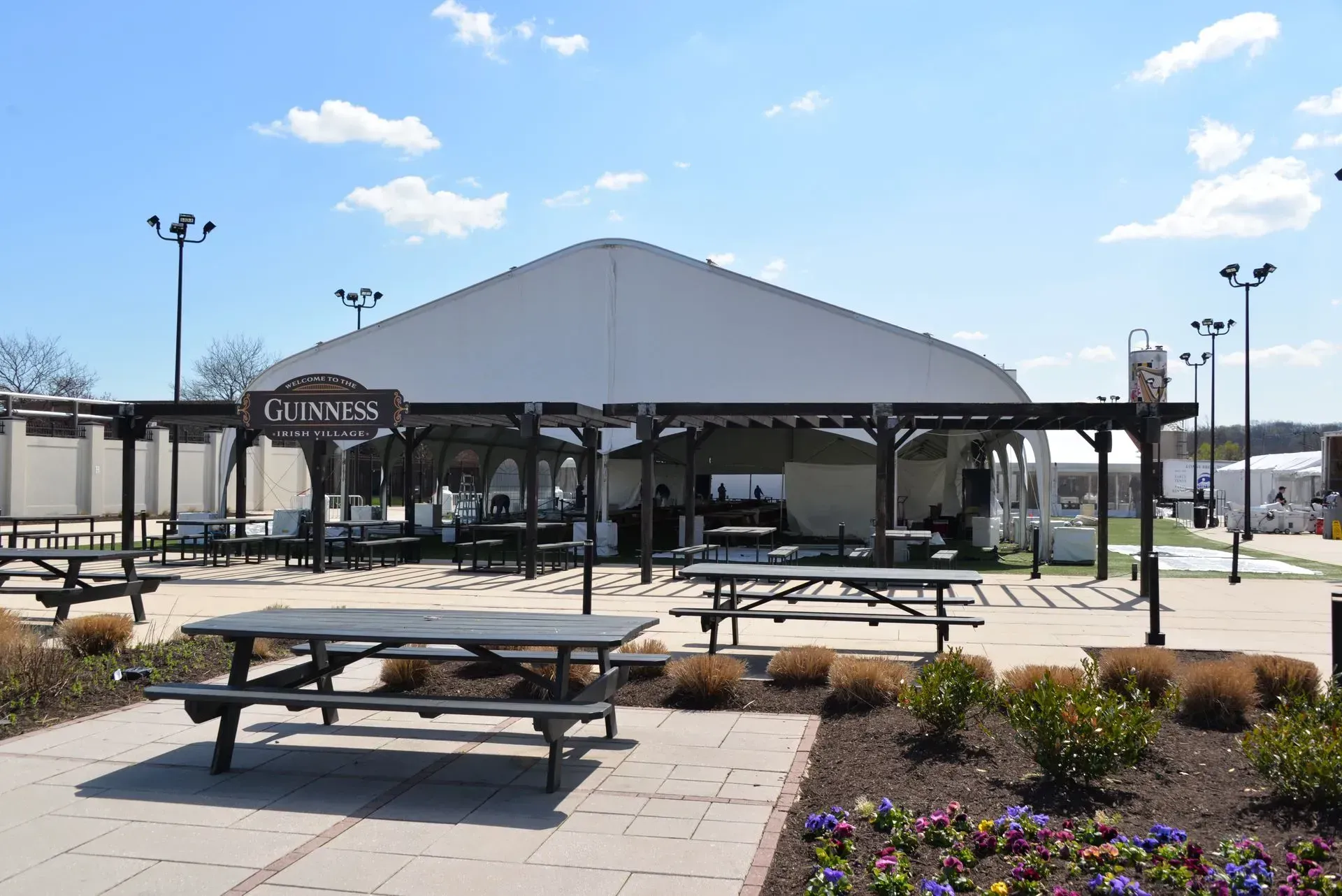 An outdoor beer garden with a large white tent, Guinness signage, and several wooden picnic tables on a sunny day.