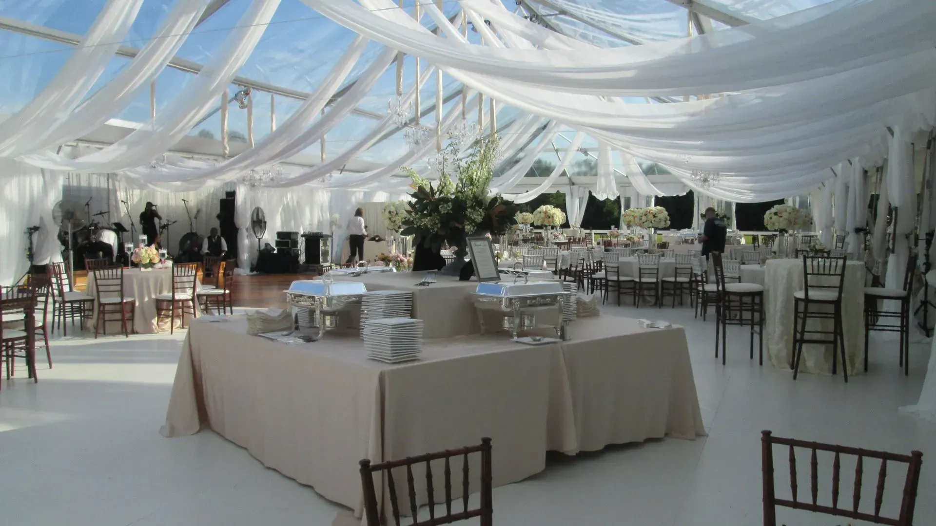 A large event tent with draped white ceiling fabric, buffet tables, and seating arranged for a formal reception.
