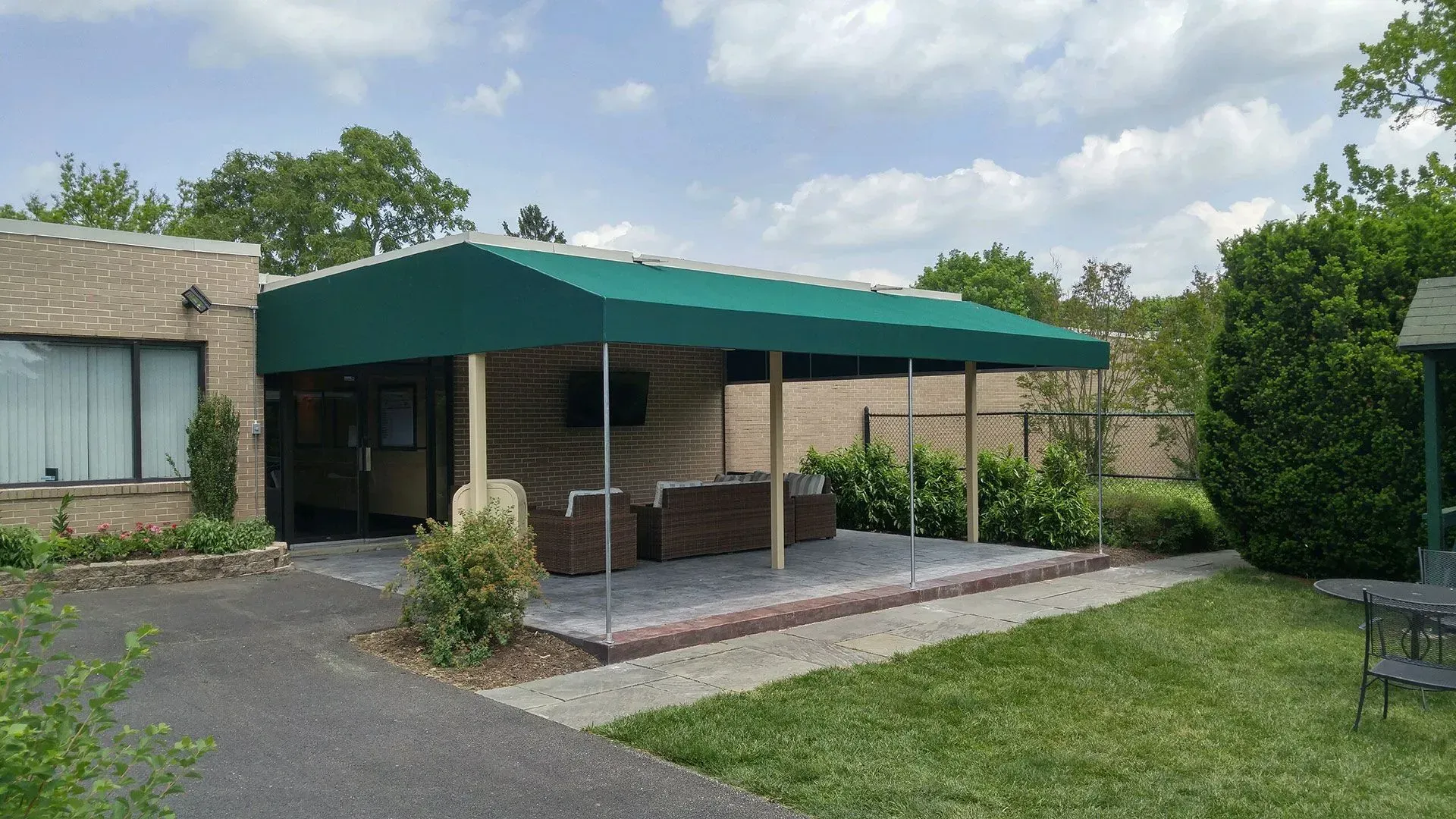 Brick patio with green canopy gazebo and outdoor seating beside a house, surrounded by lawn and shrubs