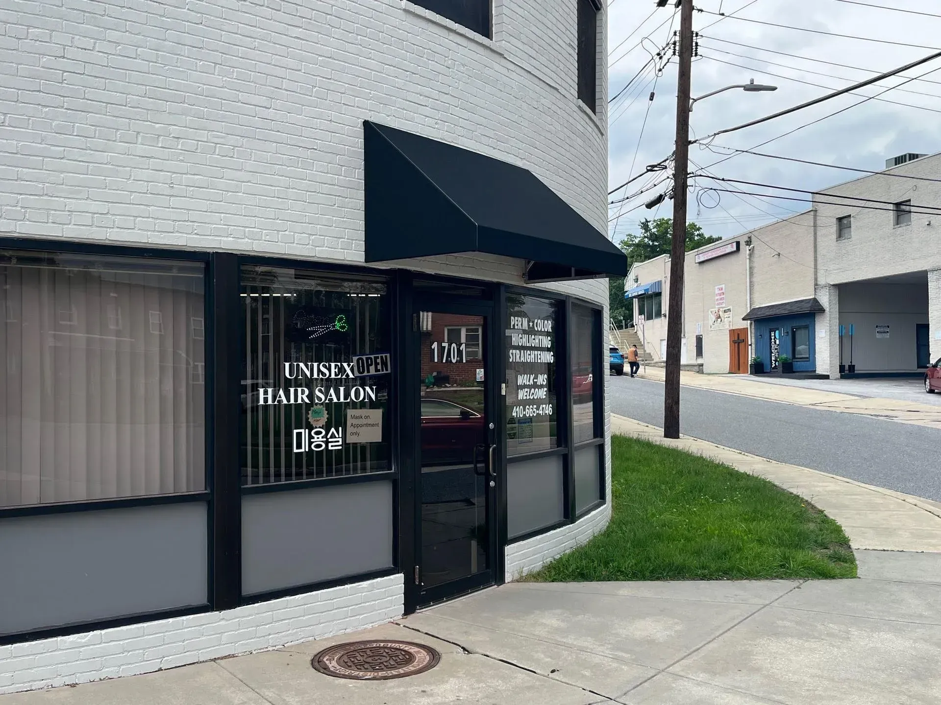 A street-level corner view of a white brick building housing a unisex hair salon with a black awning and glass door.