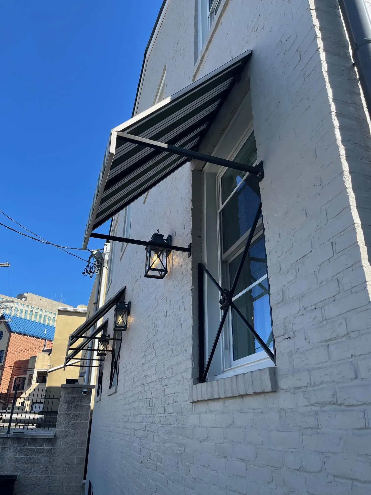 A white brick building exterior with black striped window awnings, black metal wall lanterns, and window security bars.