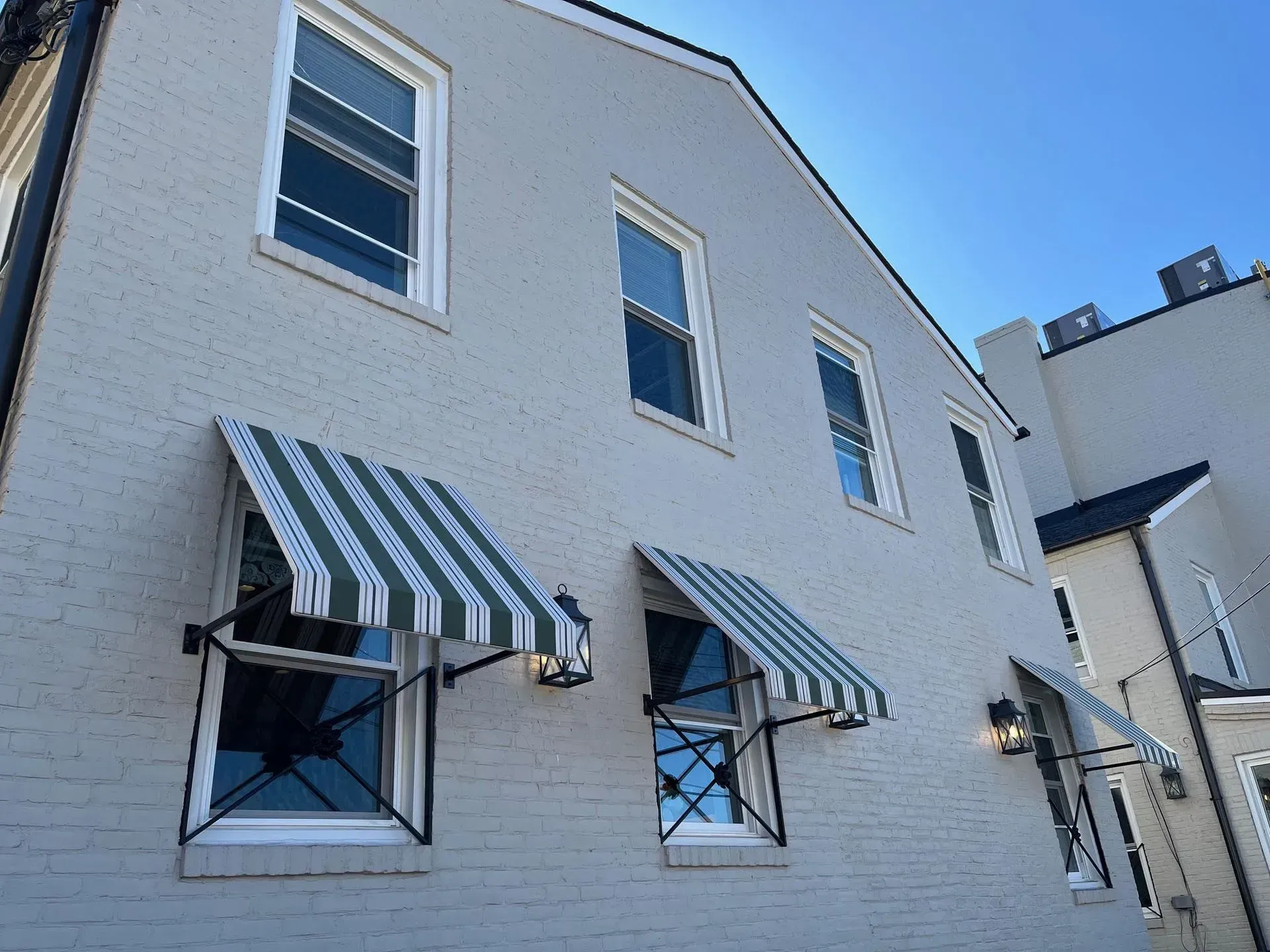 A light gray brick building with dark green and white striped awnings over three windows, viewed from a low angle.