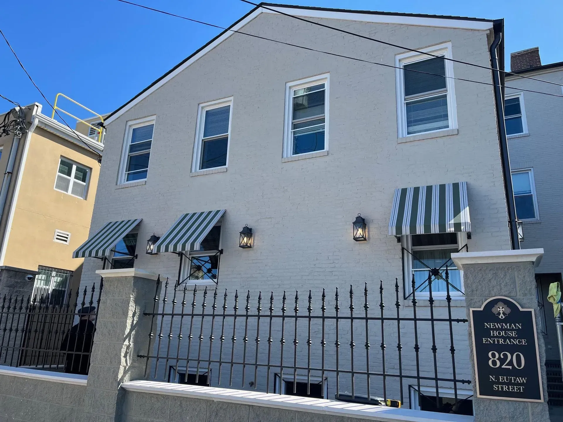 A light gray three-story building with striped awnings behind an iron fence, with a sign reading 820 near the entrance.