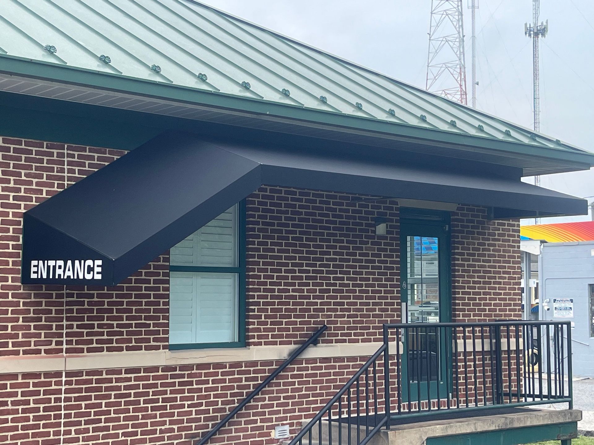 Brick building entrance with green metal roof, black railing, and white ENTRANCE sign.