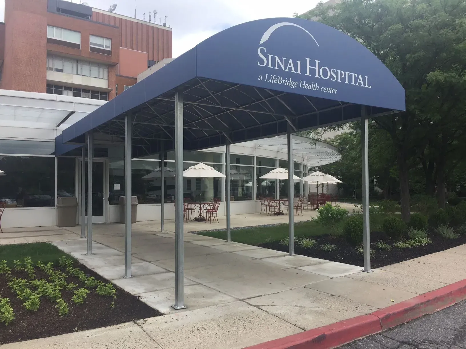 A blue entrance awning at Sinai Hospital with outdoor seating and white umbrellas on the patio.
