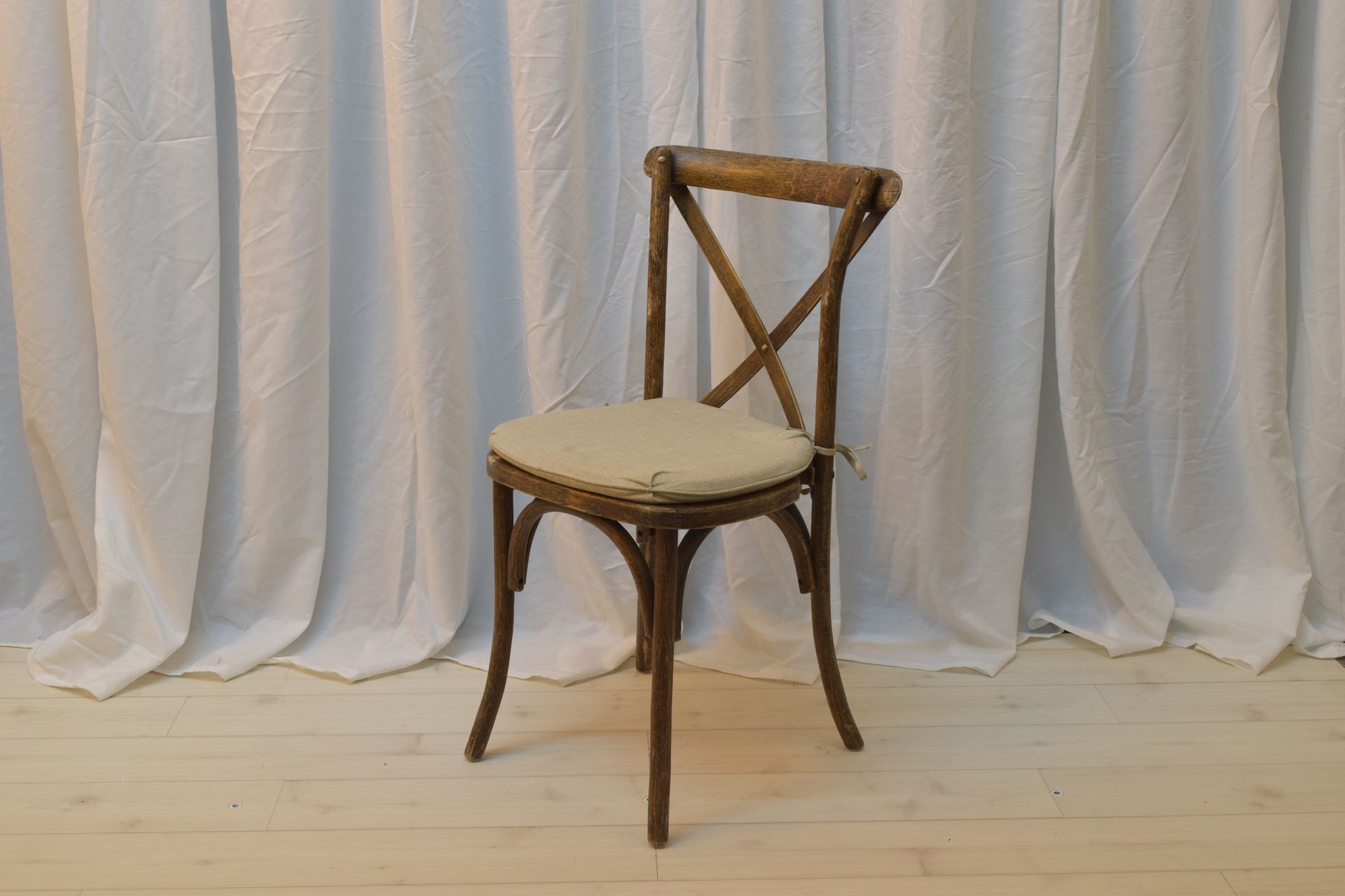 Wooden chair with cream cushion in front of a white draped backdrop