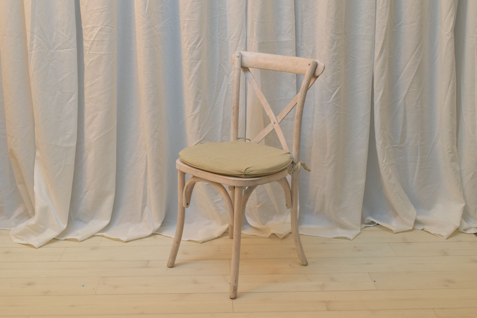 Beige wooden chair with round seat on a light wood floor in front of white curtains