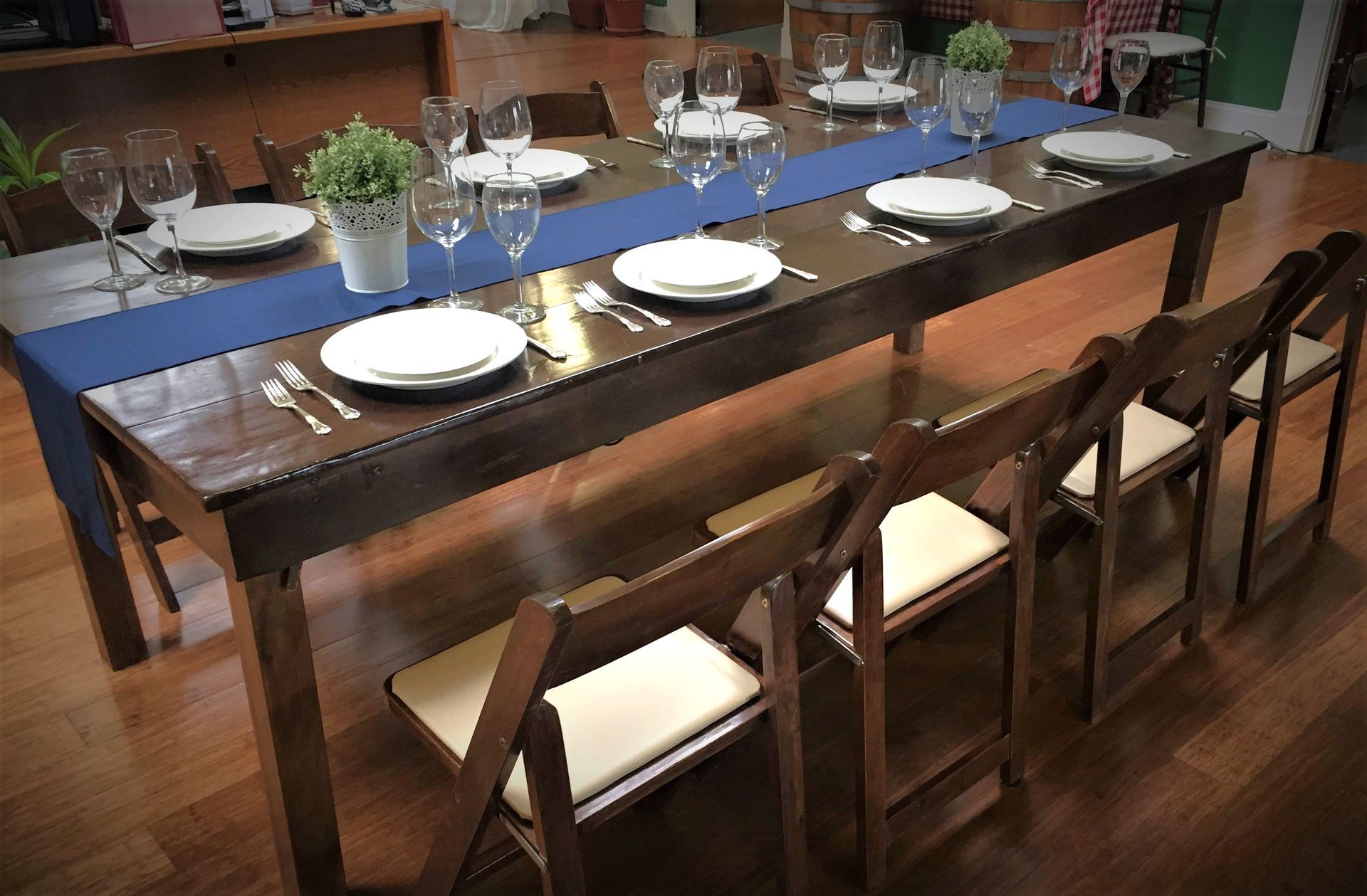 Long wooden dining table set with white plates, blue runner, and potted plants in a dining room