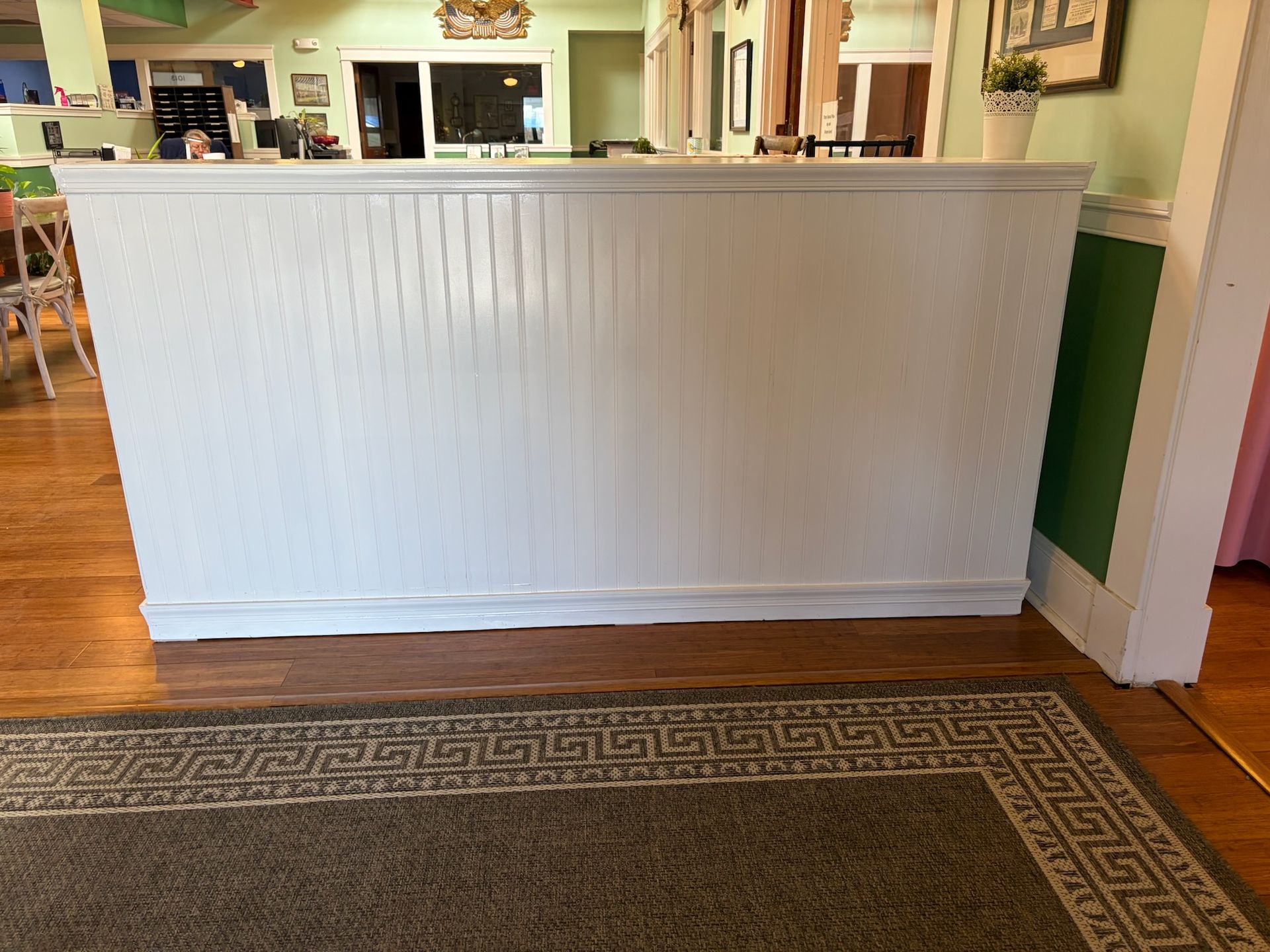 White paneled reception counter in a bright hallway with a patterned rug and wood floor