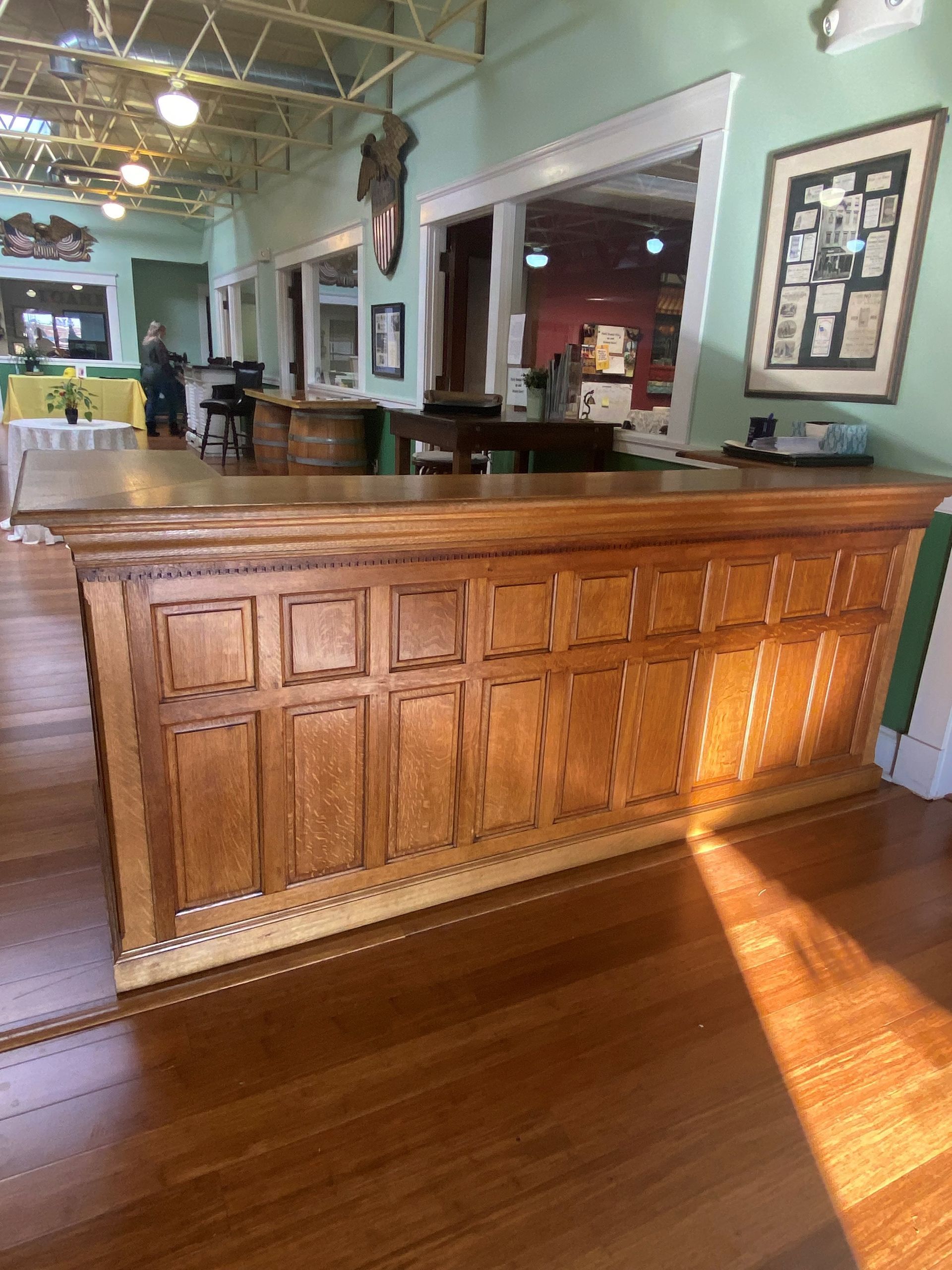 Wooden reception counter in a sunlit restaurant with green walls and framed decor
