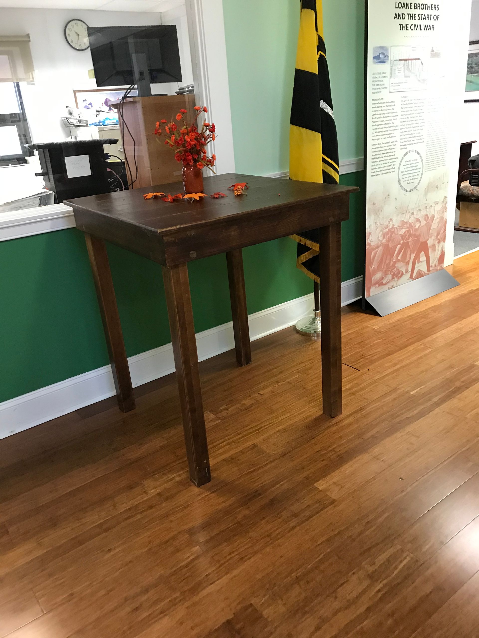 Small dark wooden table with orange decor in a room with hardwood floor and a Jamaican flag.
